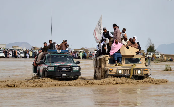 Afghan men sit atop of military vehicles as they cross through a flooded area. (SANAULLAH SEIAM/GETTY IMAGES)